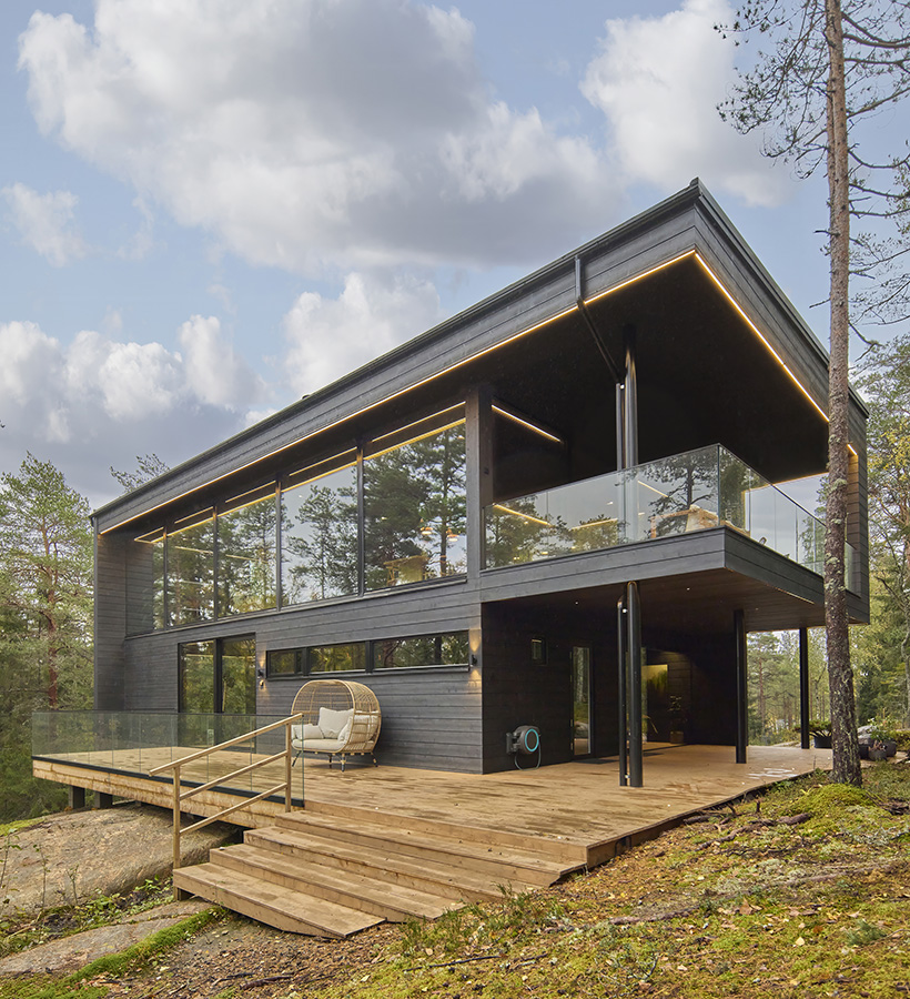 A modern black Polar Life Haus log house in a forest setting.